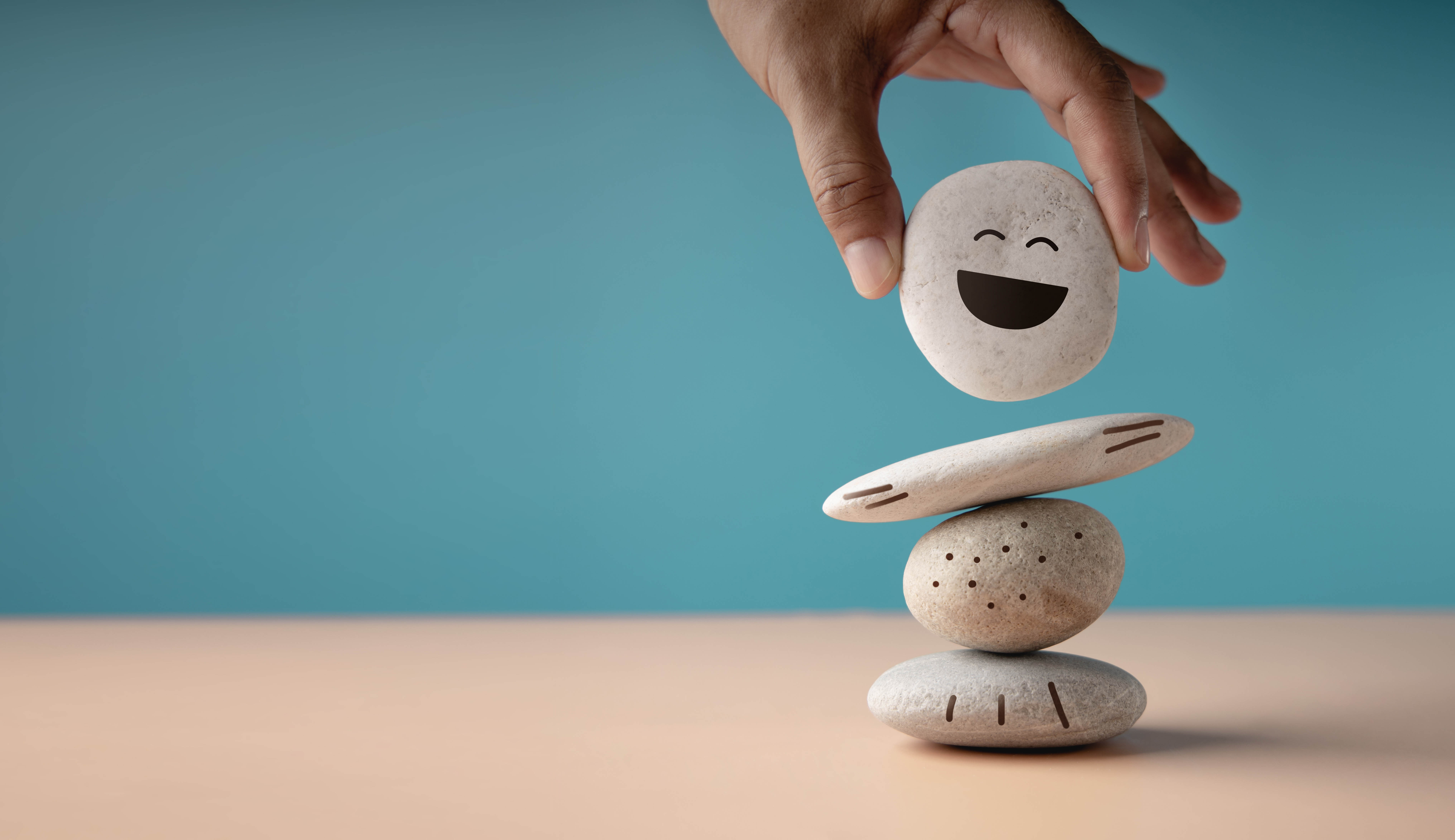 Close-up of hand stacking rocks painted with happy faces to make them balance